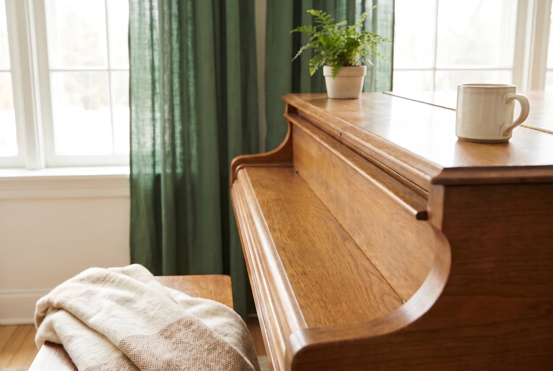 A wooden upright piano with its key cover closed beside a sunlit window.